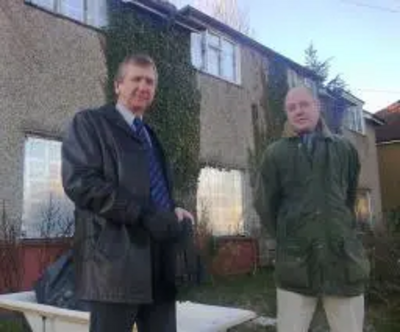 Cllrs. Graham Pooley & Ashley Final standing in front of the boarded up house