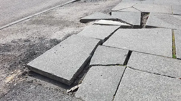 A pavement with broken and dislodged paving slabs.